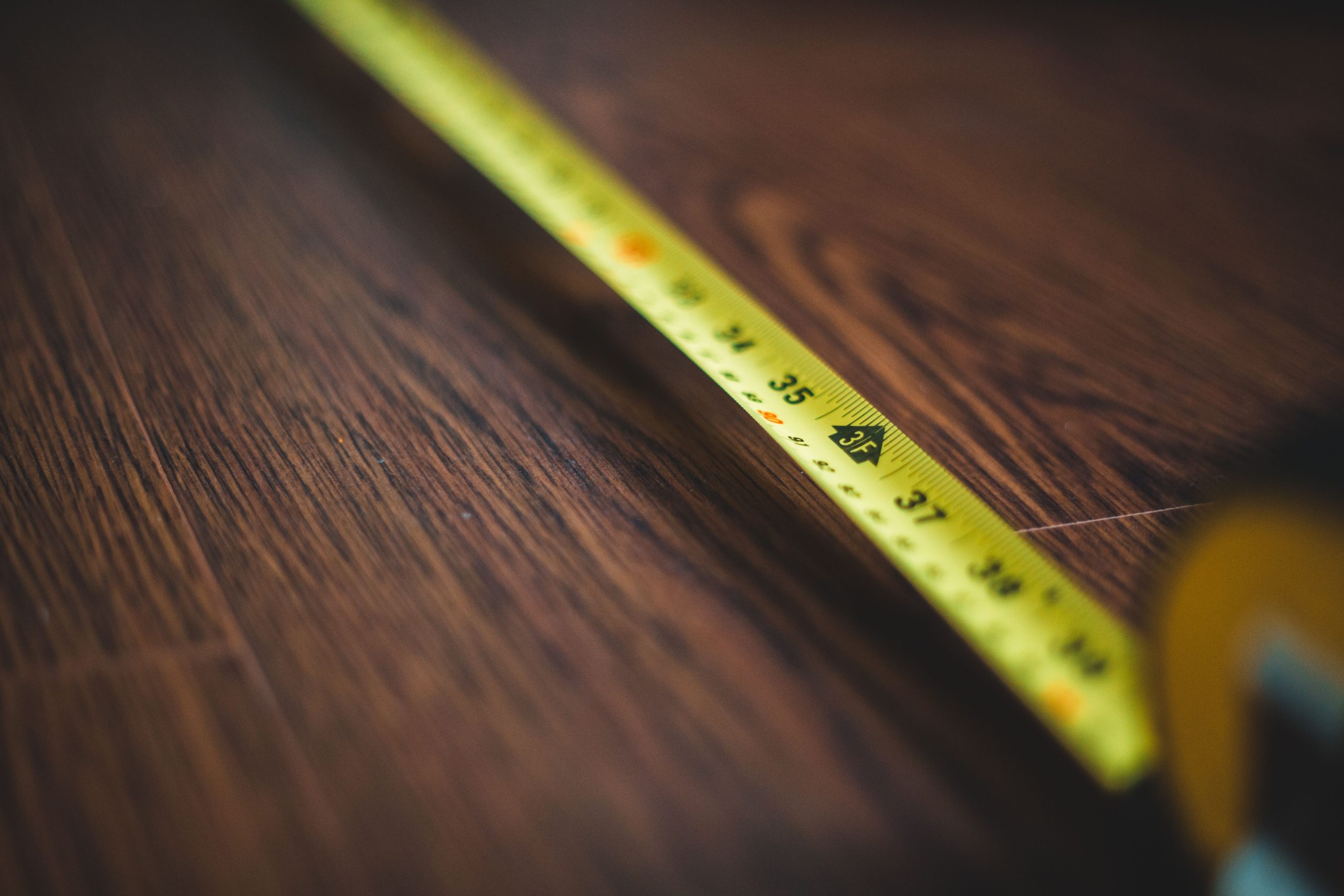 Mètre jaune mesurant plancher bois foncé